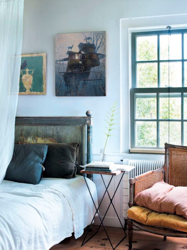 Puede incluir: Un dormitorio con una cama blanca, una cabecera de madera y una mesita de noche de metal negro. Se ve una ventana con vistas a los &aacute;rboles y una silla con un coj&iacute;n rosa. Dos cuadros enmarcados cuelgan de la pared, uno con una casa en el &aacute;rbol y el otro con un jarr&oacute;n.