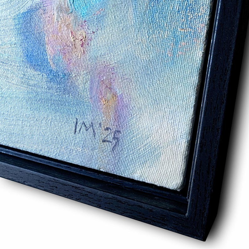 May include: An abstract oil painting with a palette of blues, purples, and creams, framed in a black wooden frame. The artwork features visible brushstrokes and the artist's initials and year, "IM '23", in the lower right corner. The painting is angled, showcasing the textured canvas.