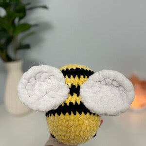 May include: A crocheted bee plush toy with yellow and black stripes and white fuzzy wings.