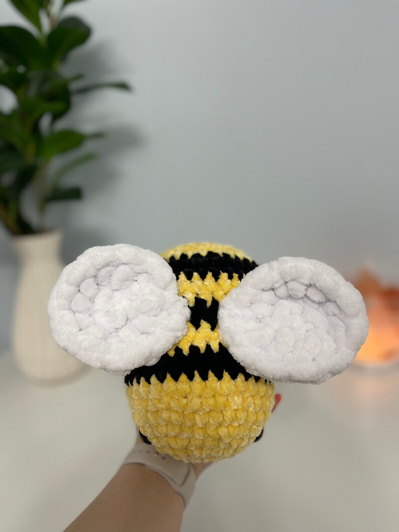 May include: A crocheted bee plush toy with yellow and black stripes and white fuzzy wings.
