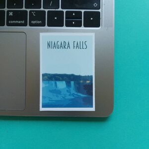 Może przedstawiać: Naklejka z niebiesko-białą ilustracją wodospadu Niagara i tekstem "NIAGARA FALLS" w ciemnoniebieskim kolorze.