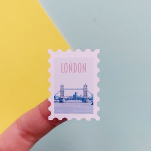 May include: A white sticker with a picture of Tower Bridge in London, England. The sticker has a scalloped edge and says "LONDON" in pink letters.
