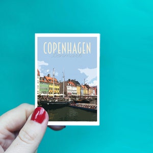 May include: A vintage-style postcard featuring a colourful illustration of Copenhagen, Denmark. The postcard shows a waterfront scene with colourful buildings, boats, and a blue sky.