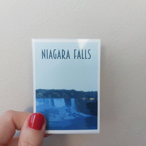 Może przedstawiać: Biała naklejka z niebieskim tłem i tekstem "NIAGARA FALLS" w kolorze czarnym. Naklejka przedstawia niebiesko-białą ilustrację wodospadu Niagara.