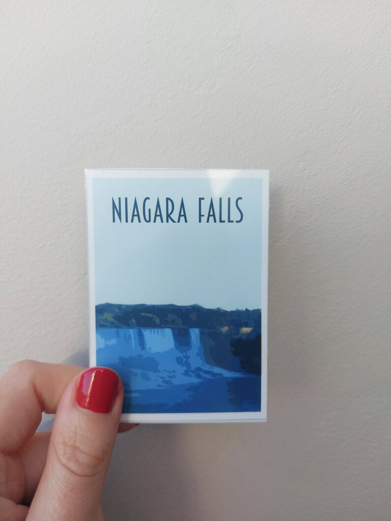 Może przedstawiać: Biała naklejka z niebieskim tłem i tekstem "NIAGARA FALLS" w kolorze czarnym. Naklejka przedstawia niebiesko-białą ilustrację wodospadu Niagara.