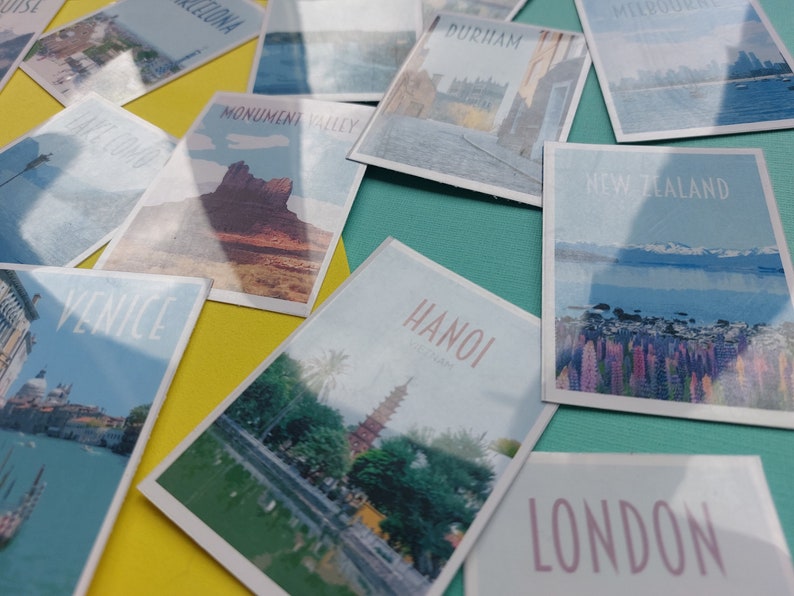 Op de afbeelding: Een verzameling vintage reisposters in postkaartstijl met verschillende bestemmingen, waaronder Monument Valley, Veneti&euml;, Hanoi, Nieuw-Zeeland, Londen en Durham. De posters zijn gerangschikt op een gele en turquoise ondergrond.