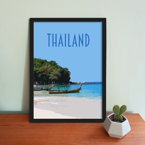 May include: A framed print of a beach scene in Thailand. The print features a blue sky, turquoise water, a sandy beach, and two longtail boats. The text "THAILAND" is printed in blue at the top of the print.