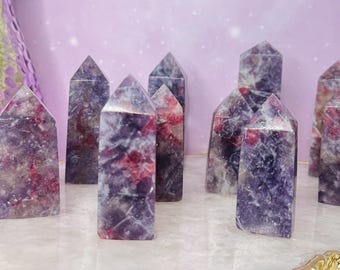 May include: A collection of purple and red crystal towers with pointed tops. The crystals have a marbled appearance, with varying shades of purple and red throughout. They are arranged on a reflective surface.