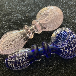 May include: Three glass pipes in the image. One is clear with white detailing, another is a light pink with white detailing, and the third is a deep blue with white detailing. The pipes have a bulbous bowl shape and a stem.