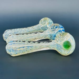 Könnte beinhalten: Drei Glaspfeifen mit einem strukturierten, gesprenkelten Design. Die Pfeifen sind hauptsächlich klar mit blauen und grünen Akzenten. Eine Pfeife hat eine grüne Kugel am Ende, eine andere blaue Punkte. Die Pfeifen sind diagonal angeordnet.
