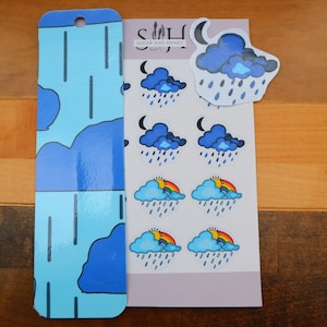 May include: A set of stickers and a bookmark featuring a weather theme. The stickers include illustrations of clouds, rain, rainbows, and moons. The bookmark is light blue with a cloud and rain design. The text "Sugar and Honey" is visible.