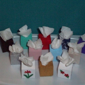 May include: Twelve miniature tissue boxes in various colors, including red, blue, green, purple, silver, and gold. Each box has a white tissue paper peeking out of the top.