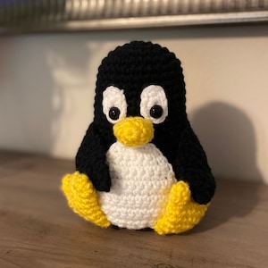 May include: A crocheted penguin toy with black and white body and yellow feet. The penguin has black eyes and a yellow beak.