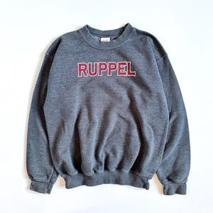 May include: A gray sweatshirt with a maroon embroidered logo that says "Ruppel".