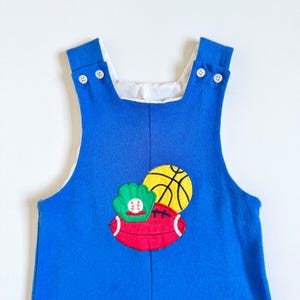 Puede incluir: Pantalón vaquero azul con ribete blanco y un diseño bordado de béisbol, baloncesto y fútbol.