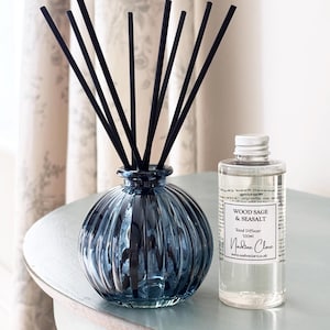 May include: A blue glass reed diffuser with black reeds and a clear bottle of Wood Sage & Seasalt fragrance. The diffuser has a ribbed design and the fragrance bottle has a white label with text.