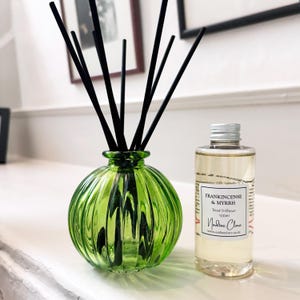 May include: A green glass reed diffuser with black reeds and a bottle of Frankincense & Myrrh fragrance. The diffuser has a ribbed design and a round shape. The fragrance bottle is clear with a silver cap.