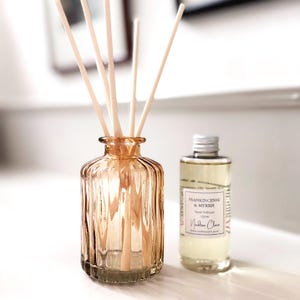 May include: An amber glass reed diffuser with wooden reeds. Beside it is a 100ml bottle of Frankincense & Myrrh reed diffuser oil. The label includes the text "Nadine Clare".