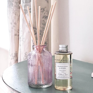 May include: A pink glass reed diffuser with wooden sticks and a bottle of Frankincense & Myrrh Reed Diffuser 100ml. The diffuser has a textured pattern. The bottle has a silver cap and a white label with black text.