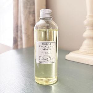 May include: A clear glass bottle filled with pale yellow reed diffuser oil, featuring a silver screw cap. The white label reads NEROLI LAVENDER & JASMINE, Reed Diffuser, 100ml, Nadine Clare, and www.nadineclare.co.uk in black text.