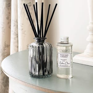 May include: A silver glass reed diffuser with black reeds and a clear bottle of Wood Sage & Seasalt fragrance. The diffuser is on a light blue table, creating a calming aesthetic.