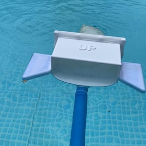Könnte beinhalten: Ein weißer Poolskimmer mit blauem Griff ist in einem Pool. Auf dem Skimmer steht das Wort "UP". Das Poolwasser ist hellblau.