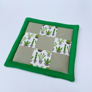 Peut inclure: Un dessous de plat matelassé vert et blanc avec un motif de cactus. Le dessous de plat est fait de tissu et a une bordure verte.