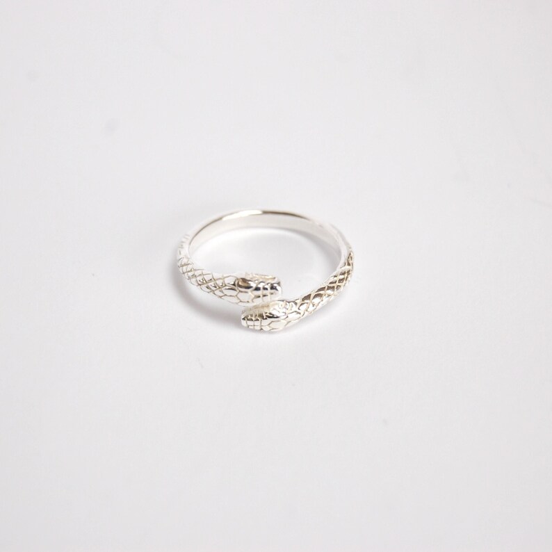 May include: A silver ring with a double snake design. The snakes are intertwined and have textured scales.