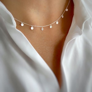 Può includere: Una collana d'argento con una catena delicata e piccoli ciondoli rotondi.
