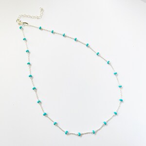 Op de afbeelding: Een delicate zilveren ketting met kleine, ronde turquoise kralen verdeeld over een fijne ketting. De ketting heeft een kreeftsluiting en wordt getoond tegen een witte achtergrond. Dit sieraad is geschikt voor dagelijks gebruik.