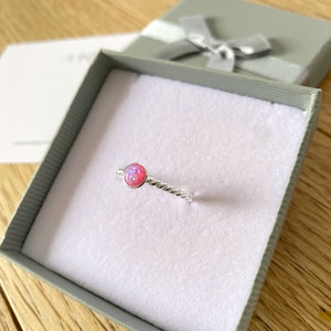 May include: A silver ring with a pink opal gemstone set in a twisted band. The ring is displayed in a small gift box.