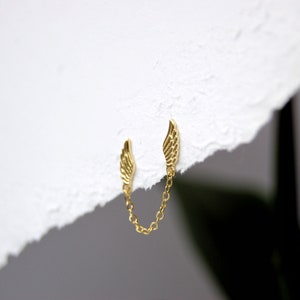 May include: A pair of gold wing earrings connected by a delicate gold chain.