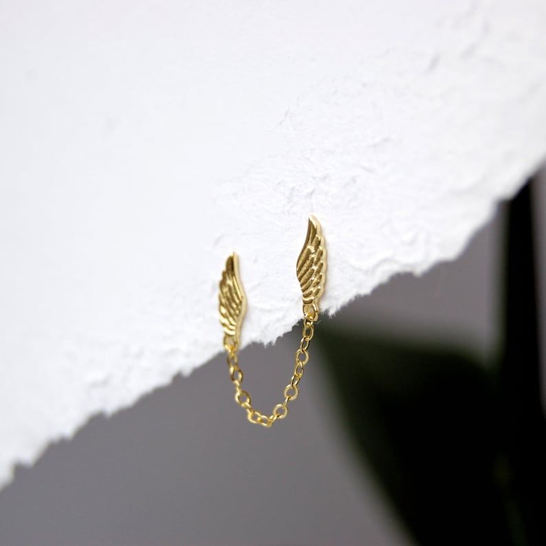 May include: A pair of gold wing earrings connected by a delicate gold chain.
