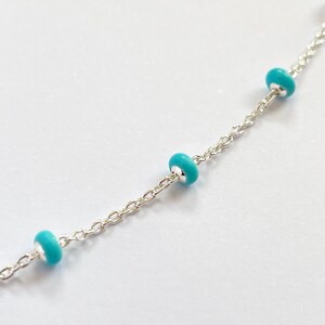 Op de afbeelding: Een delicate zilveren ketting met drie turquoise kralen gelijkmatig verdeeld over de lengte. De kralen hebben een levendige, opvallende kleur en de ketting heeft een fijn, gedetailleerd schakelpatroon.