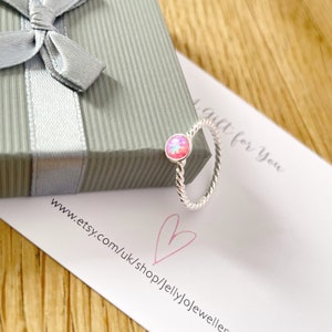 May include: A silver ring with a pink opal gemstone. The ring is twisted and has a delicate design. The ring is on a white card with the text "a gift for you" and a website address.