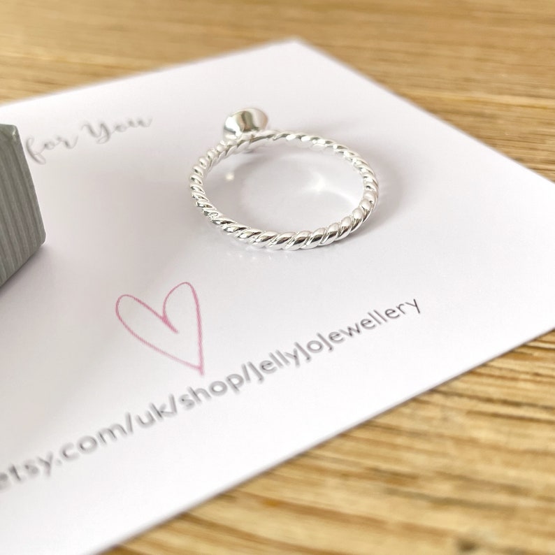 May include: A silver ring with a twisted band. The ring is on a white card with the text "etsy.com/uk/shop/jellyjojewellery" printed on it.