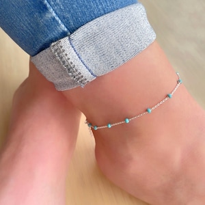 May include: A silver chain anklet with small turquoise beads. The anklet is on a person's ankle.