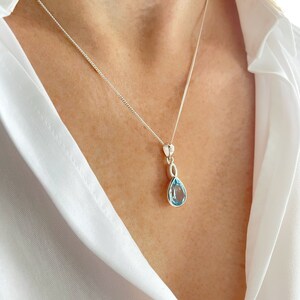 May include: A silver chain necklace with a teardrop-shaped blue topaz pendant.