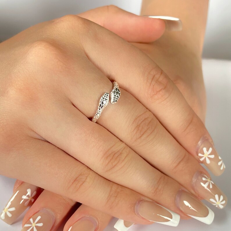 May include: A silver snake ring with two snake heads facing each other. The ring is on a person's finger.