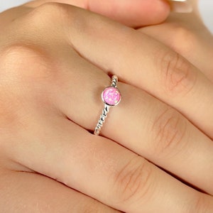 May include: A silver ring with a pink opal gemstone. The ring has a twisted band.