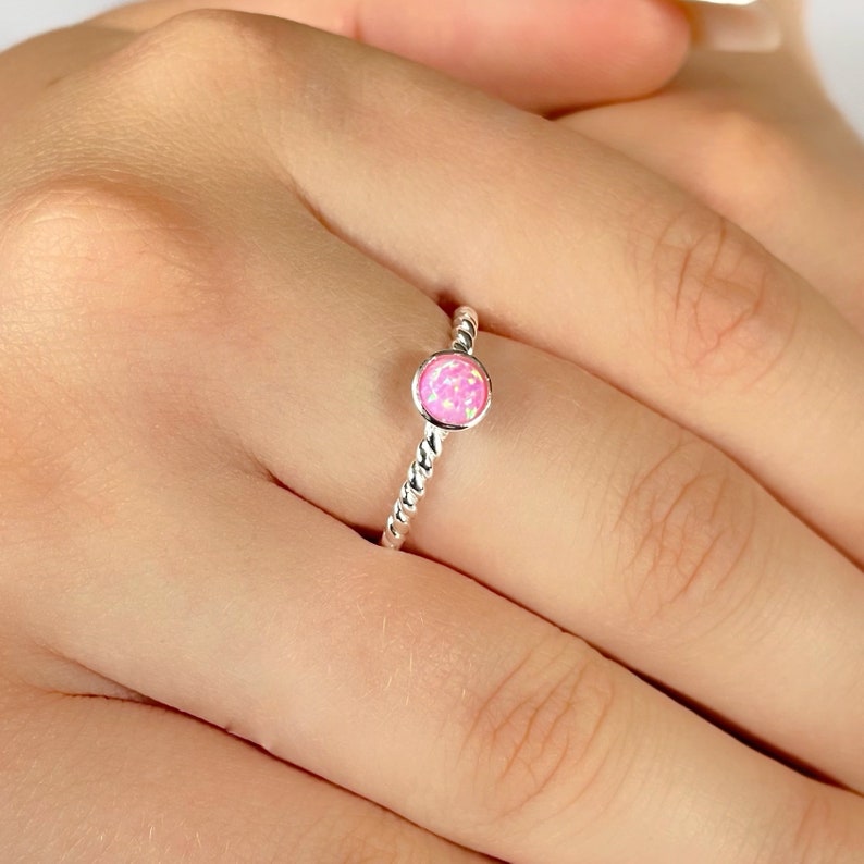 May include: A silver ring with a pink opal gemstone. The ring has a twisted band.