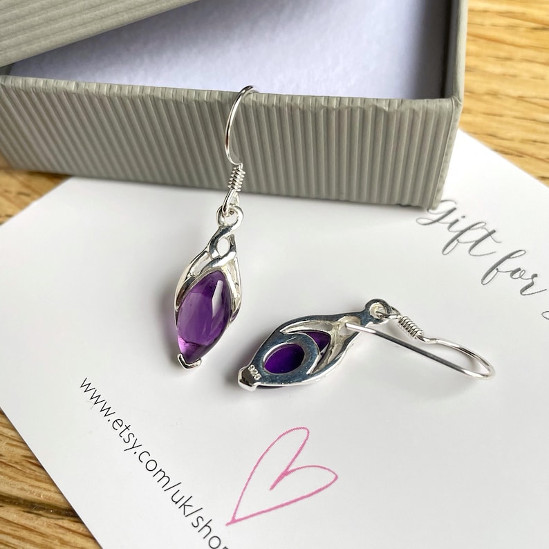 Op de afbeelding: Een paar oorbellen van sterling zilver met paarse amethiststenen. De oorbellen hebben een delicaat, ingewikkeld ontwerp en zijn perfect voor dagelijks gebruik.