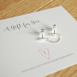 May include: A gift card with the text "A gift for you" written in cursive. A pair of silver earrings with a small wing design are displayed on the card. The earrings are connected by a delicate silver chain.