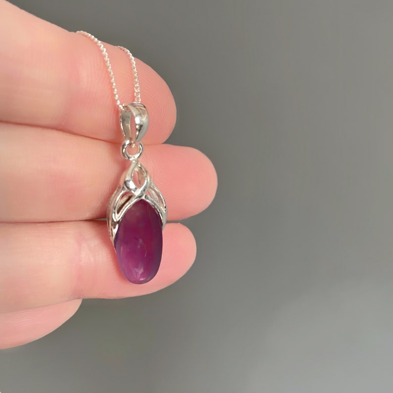 Op de afbeelding: Een zilveren ketting met een hanger met een paarse edelsteen. De hanger heeft een delicaat, ingewikkeld ontwerp.