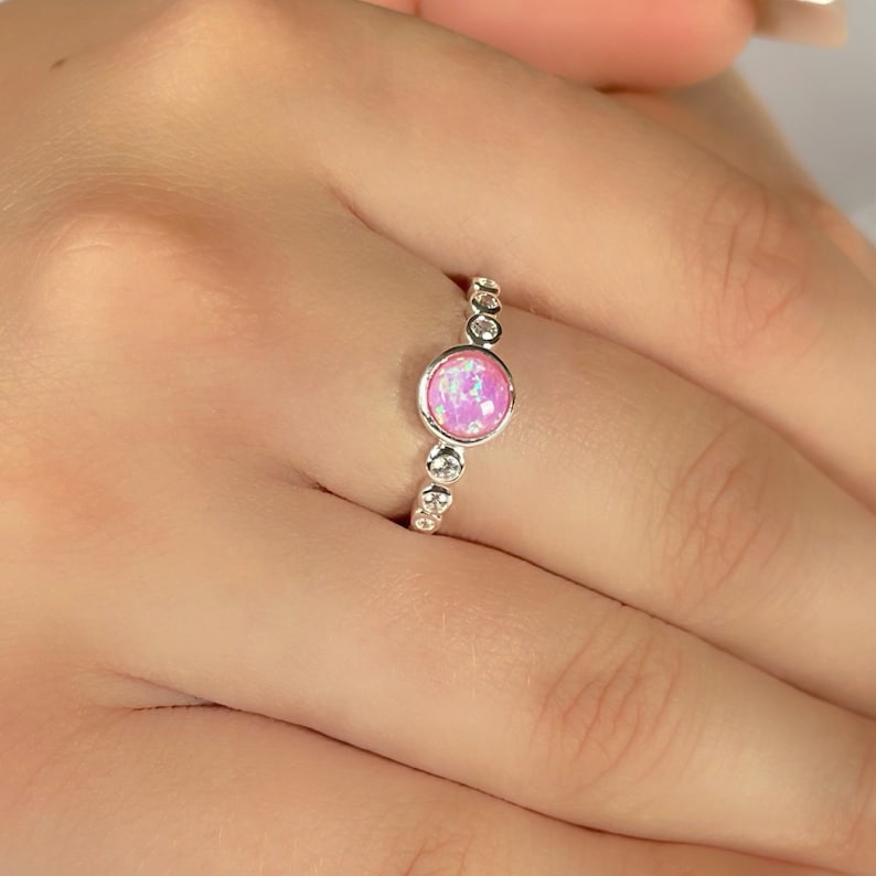 Op de afbeelding: Een zilveren ring met een roze opaal-edelsteen omringd door kleinere heldere stenen.