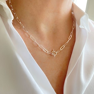 May include: A silver chain necklace with a toggle clasp. The chain is made of linked oval shapes.