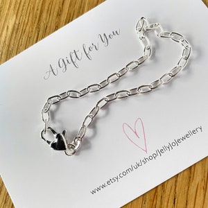 Puede incluir: Un brazalete de cadena plateada con un cierre en forma de corazón, presentado en una tarjeta blanca. La tarjeta tiene el texto "A Gift for You" y un corazón rosa. La URL de la tienda Etsy es visible.