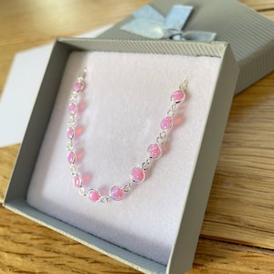 Peut inclure: Un bracelet à chaîne en argent orné de pierres rondes rose pâle, semblables à des opales, serties dans des chatons métalliques individuels. Le bracelet est présenté dans une boîte cadeau carrée grise doublée de tissu rose pâle.