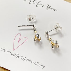 Op de afbeelding: Een paar zilveren oorbellen met een gouden bloementje. De oorbellen liggen op een witte kaart met de tekst "Gift for you" en "uk/shop/jellyjojewellery".