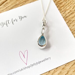 May include: A silver necklace with a teardrop-shaped pendant featuring a light blue gemstone. The pendant has a delicate, twisted design. The necklace is displayed on a white card with the text "gift for you" and a pink heart.